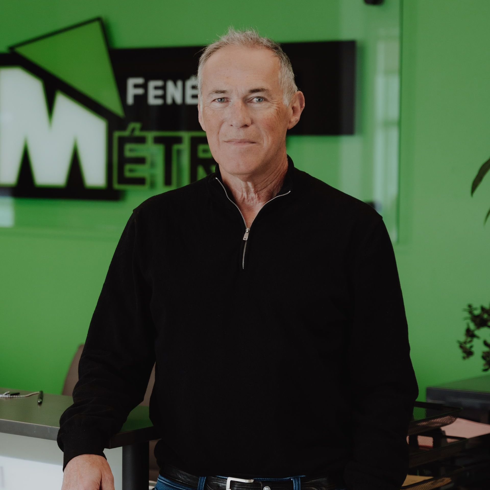 Un homme en pull noir se tient devant le panneau vert Metro Fenêtres.