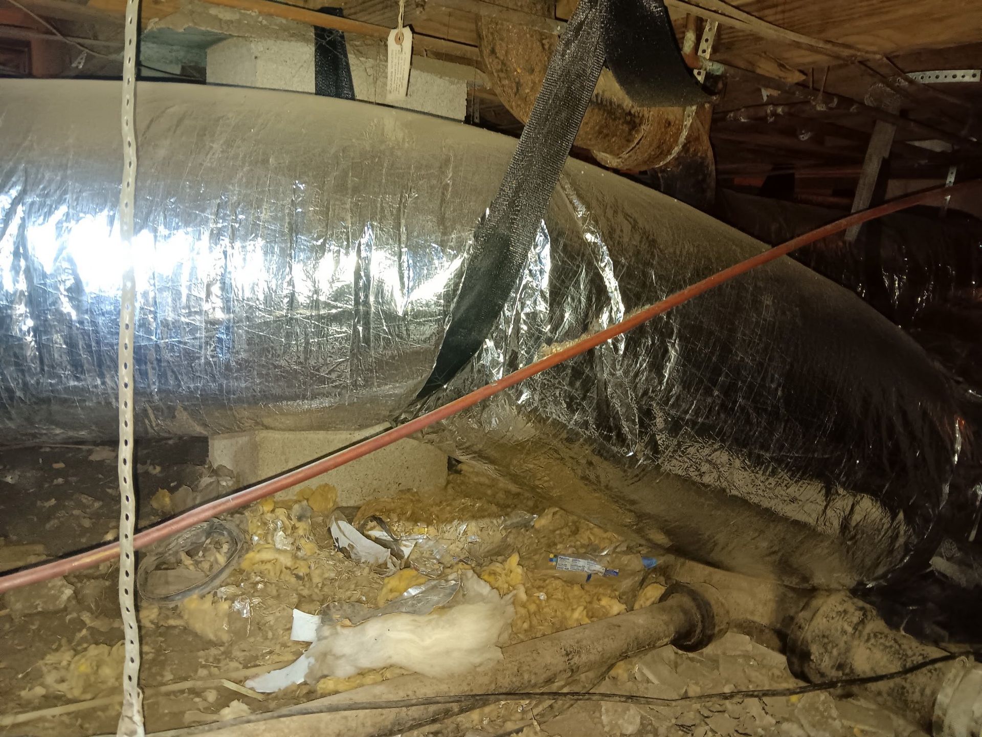 A crawl space with a lot of pipes and wires coming out of it.