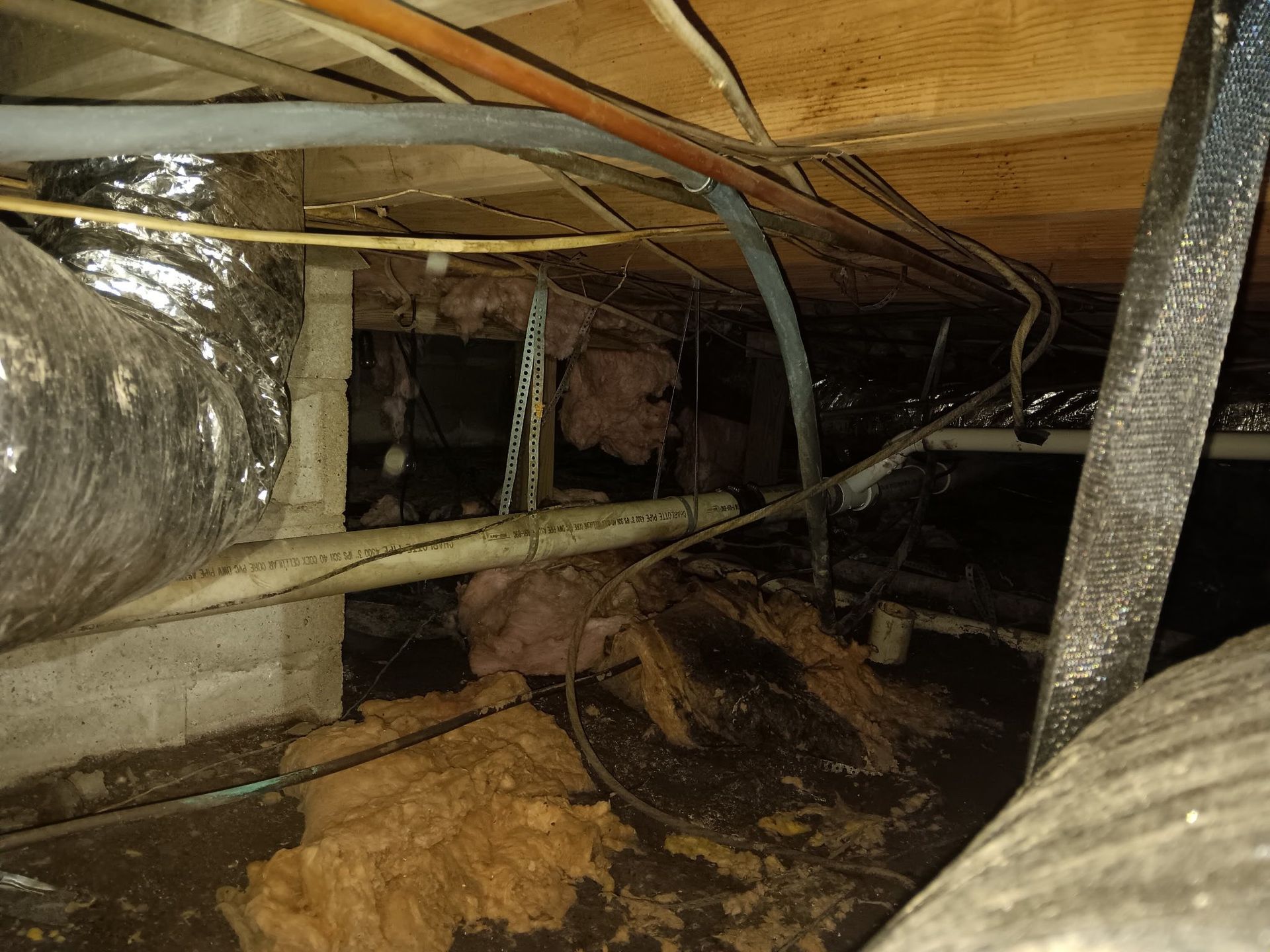 A crawl space with a lot of pipes and wires coming out of it.