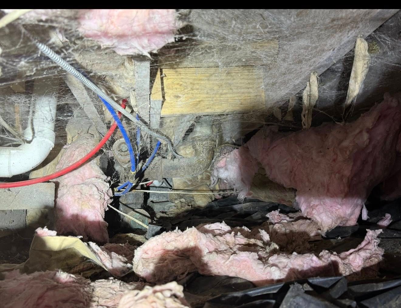 Pink insulation and wires in a crawl space; wood beams and a pipe visible.
