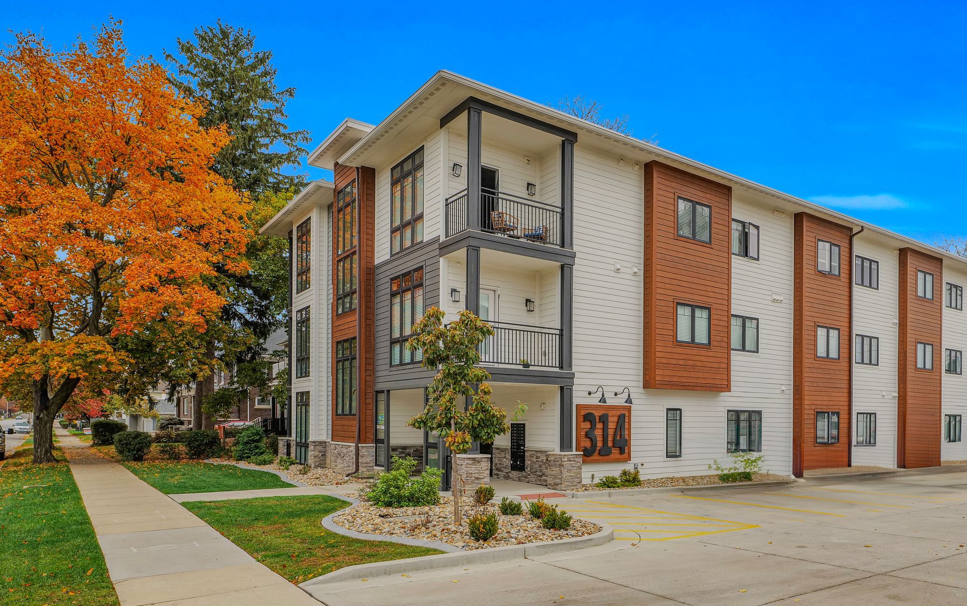 Photo showing a 3 story building with a sidewalk and a parking lot