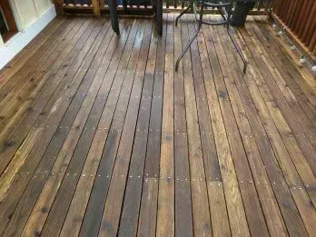 Wooden deck with various brown hues, with furniture visible in the background.