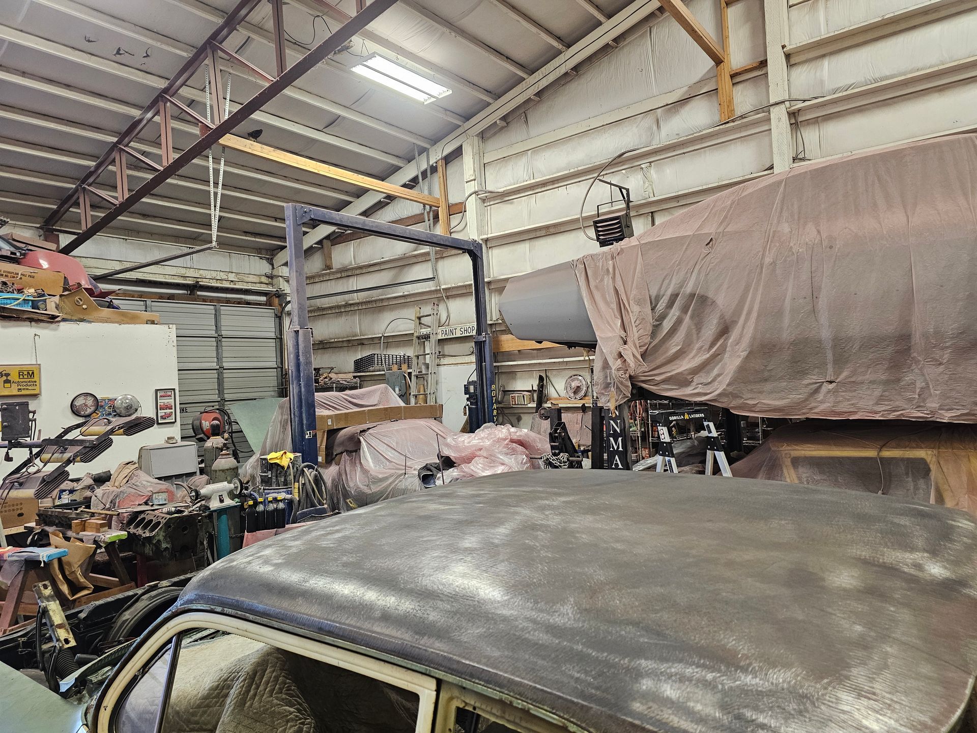An interior garage with a classic car roof in the foreground. The space is cluttered with tools and other items.