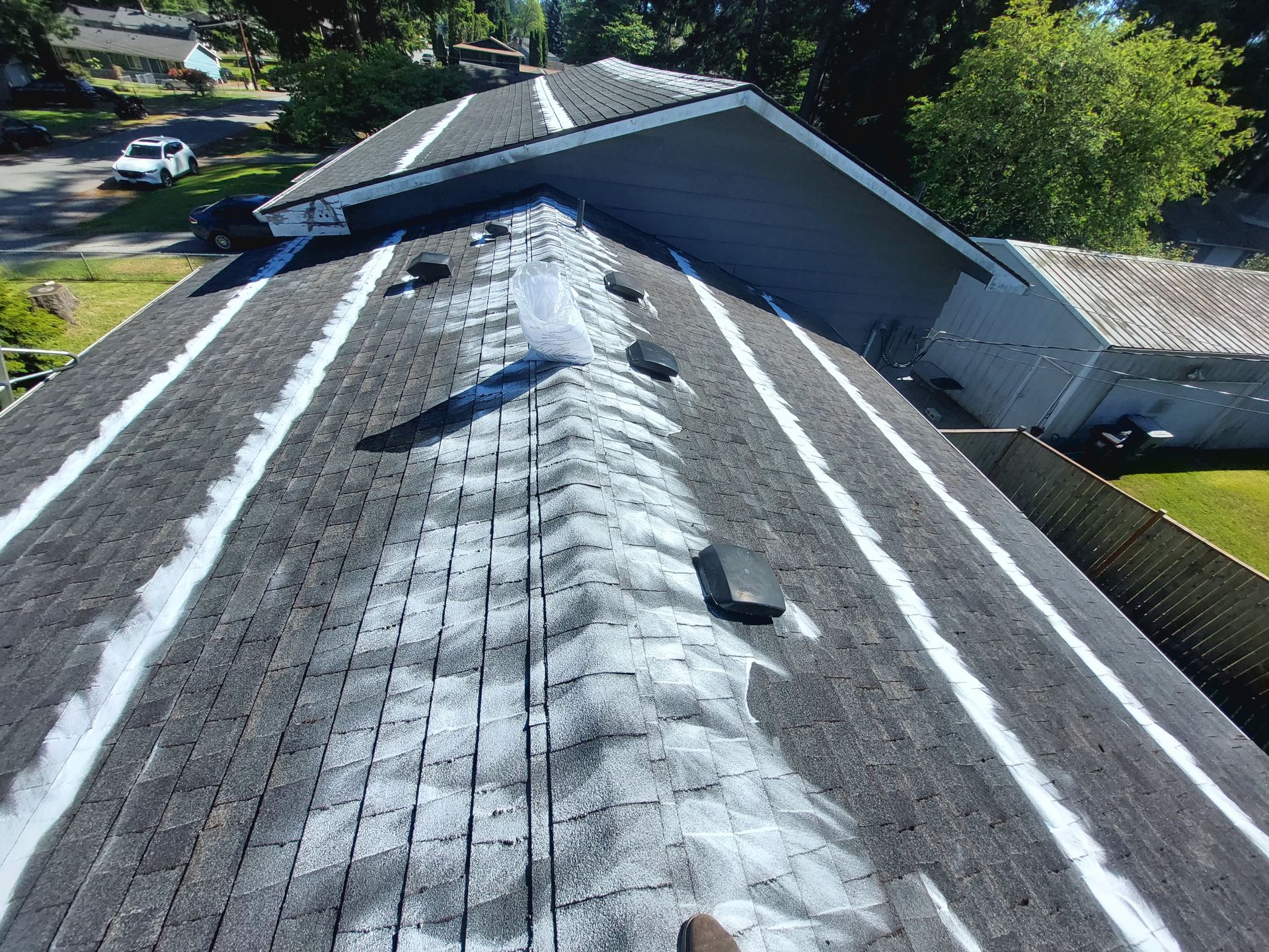 Overhead view of a dark asphalt shingle roof with white streaks and a portion of surrounding houses and yard.