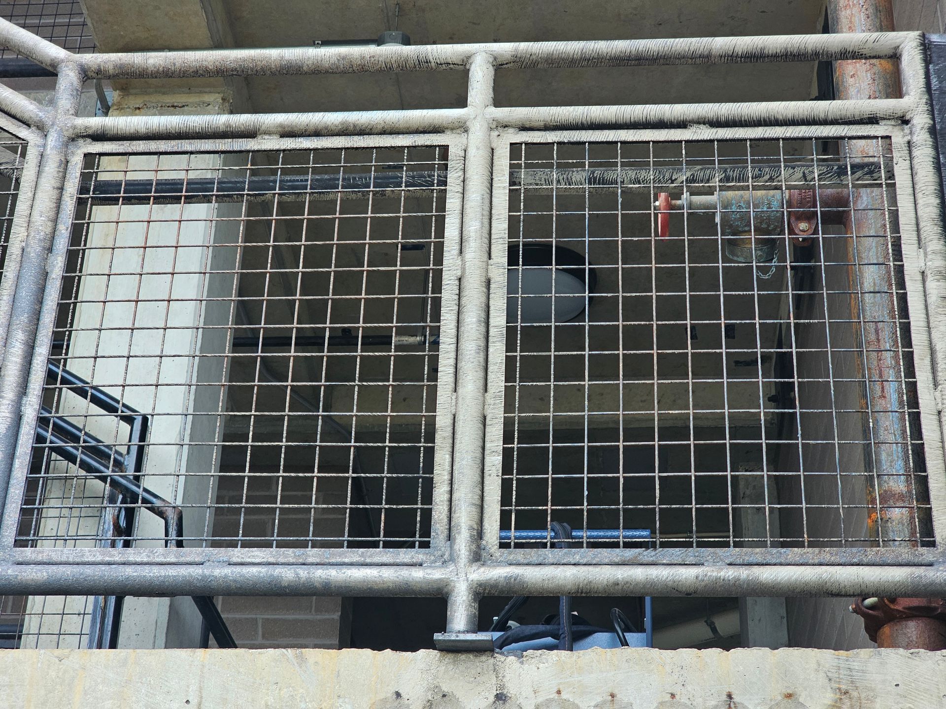Metal grate on a building, blocking a stairwell. Gray and tan colors.