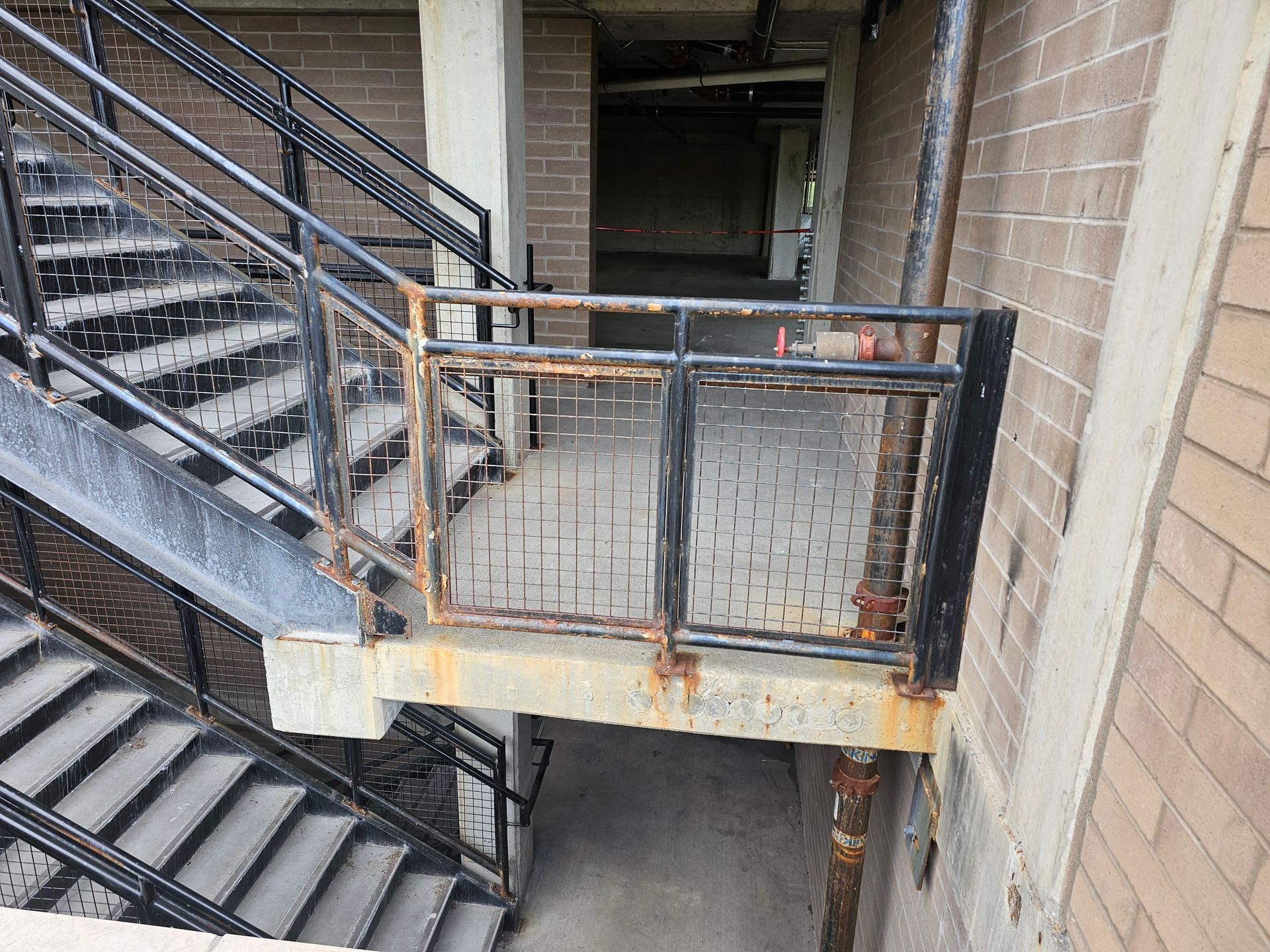 Exterior metal stairwell with a rusty railing, next to a brick building.
