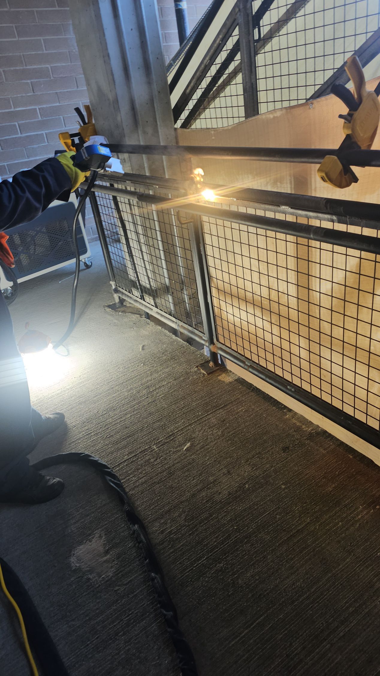 Person welding metal fencing outdoors. Sparks fly, visible blue and yellow light.