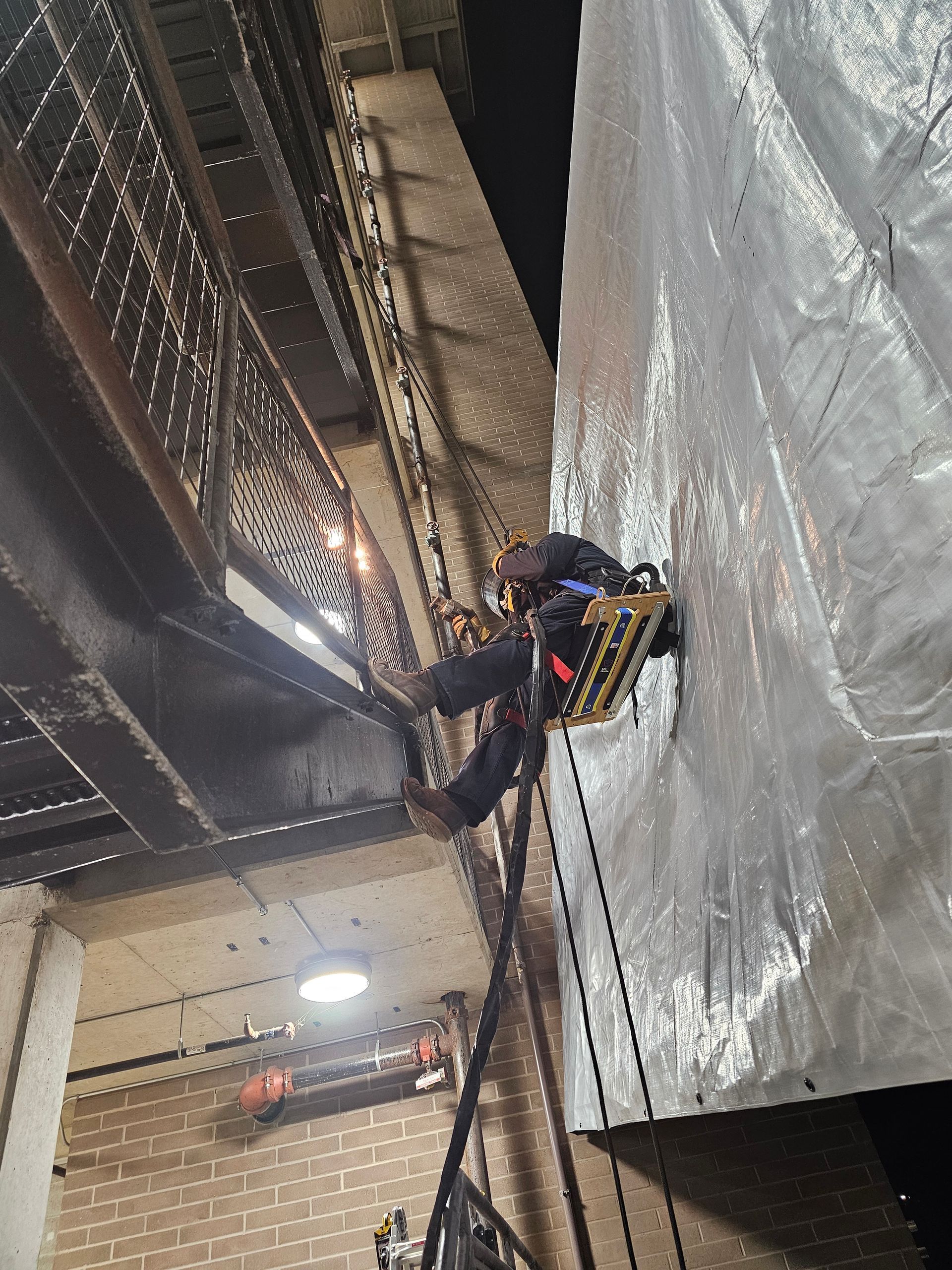 Person rappelling down a dark wall next to a metal staircase, with a safety harness and equipment.