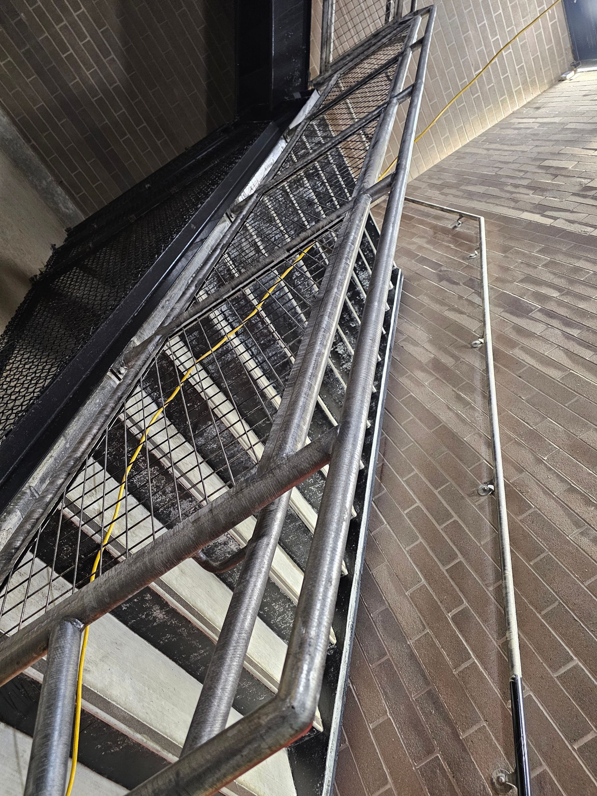 Metal staircase ascending a brick-lined tower. Handrails and safety netting visible.