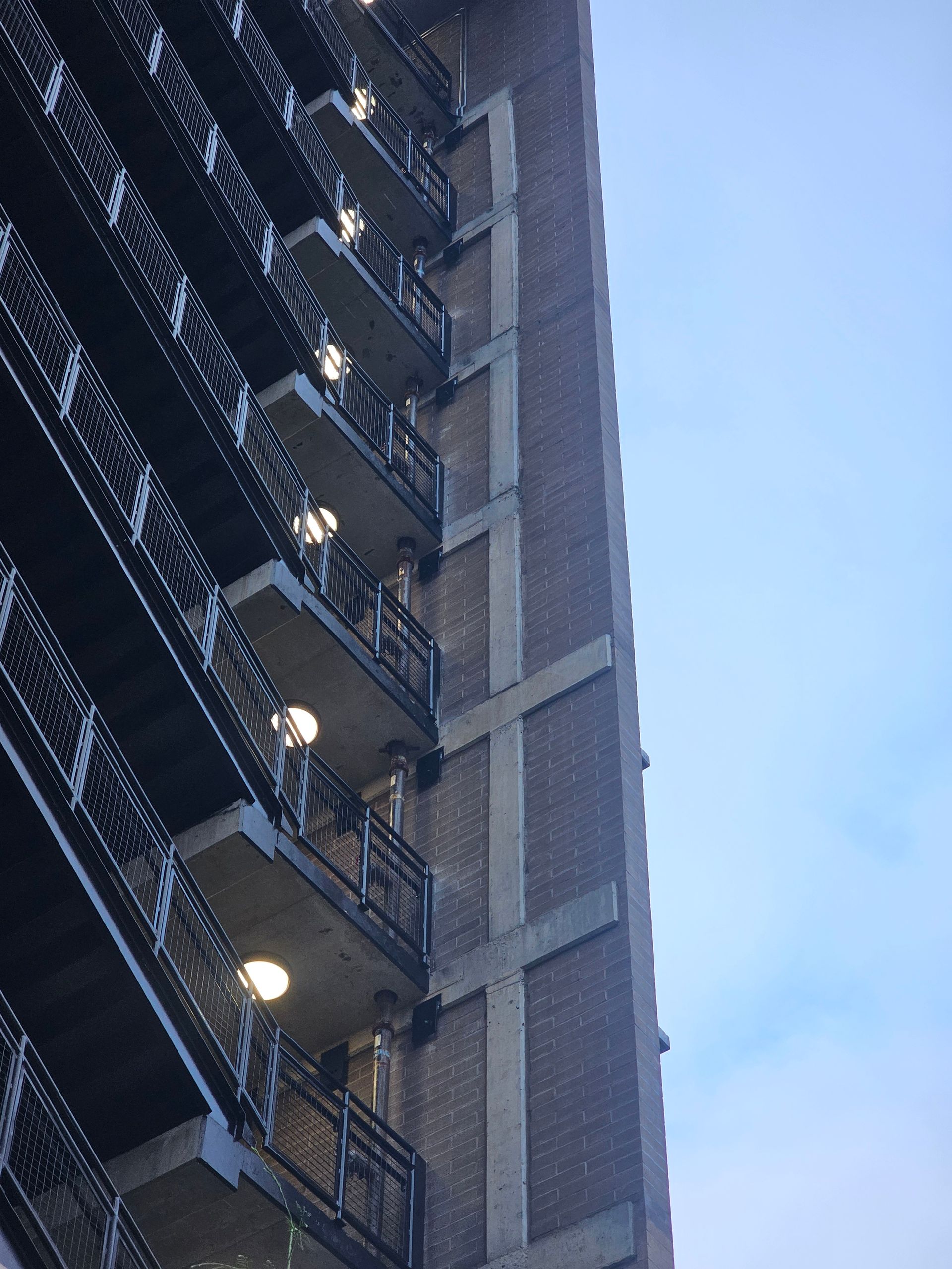Tall brick building with balconies, against a blue sky.