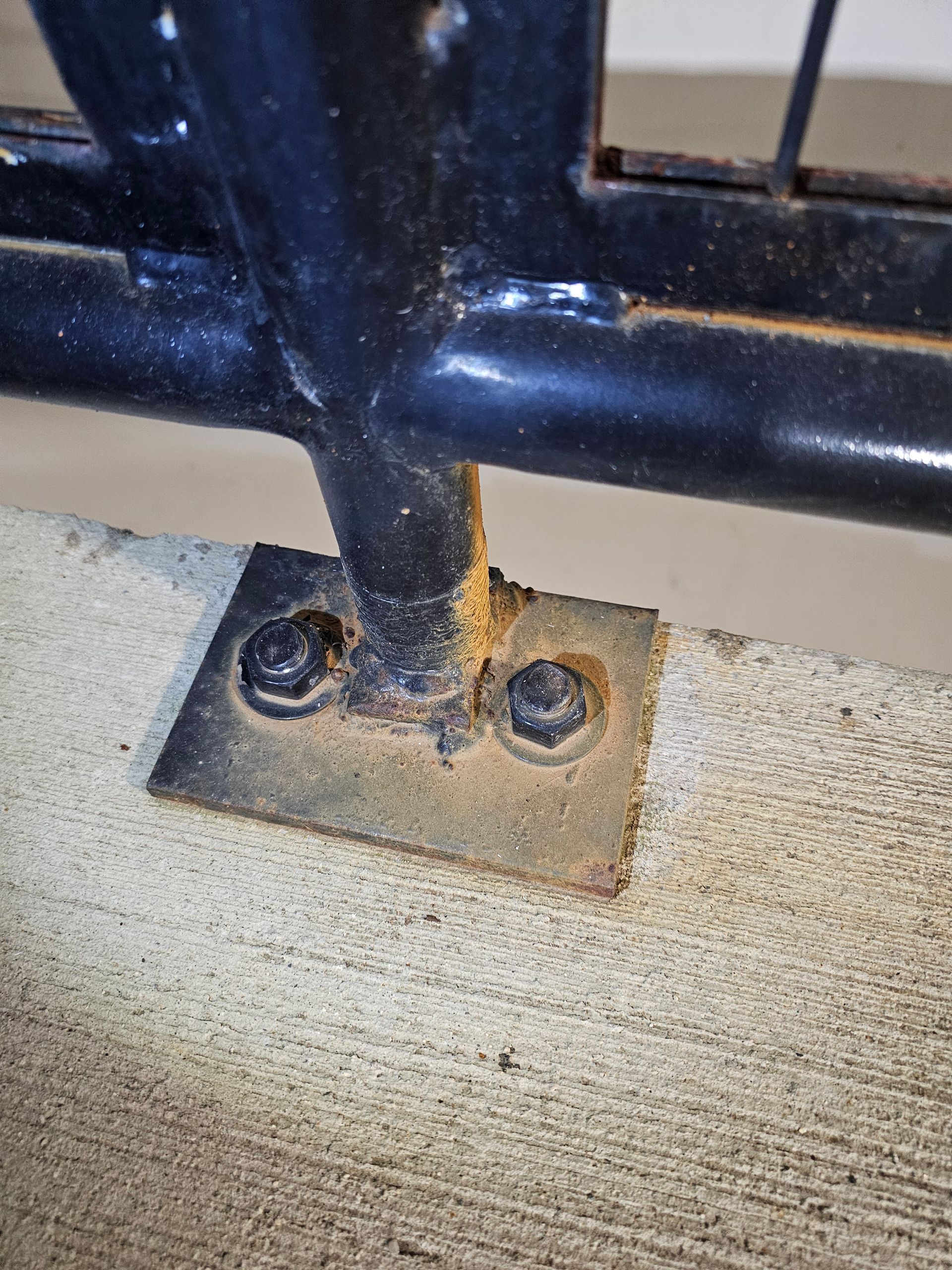 Black metal railing attached to concrete with rusty bolts.