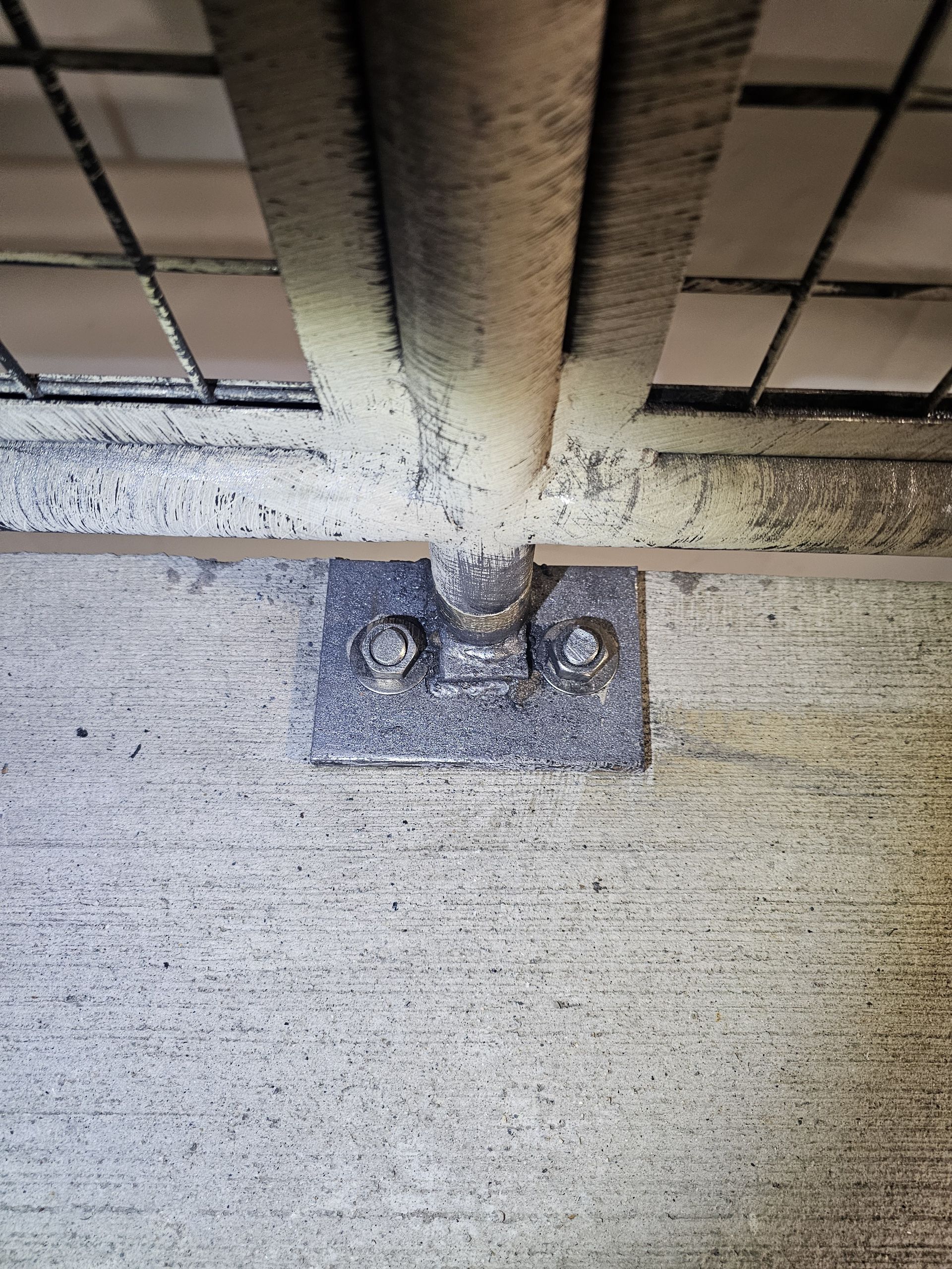 Metal bracket securing a horizontal bar and wire mesh to a concrete surface.