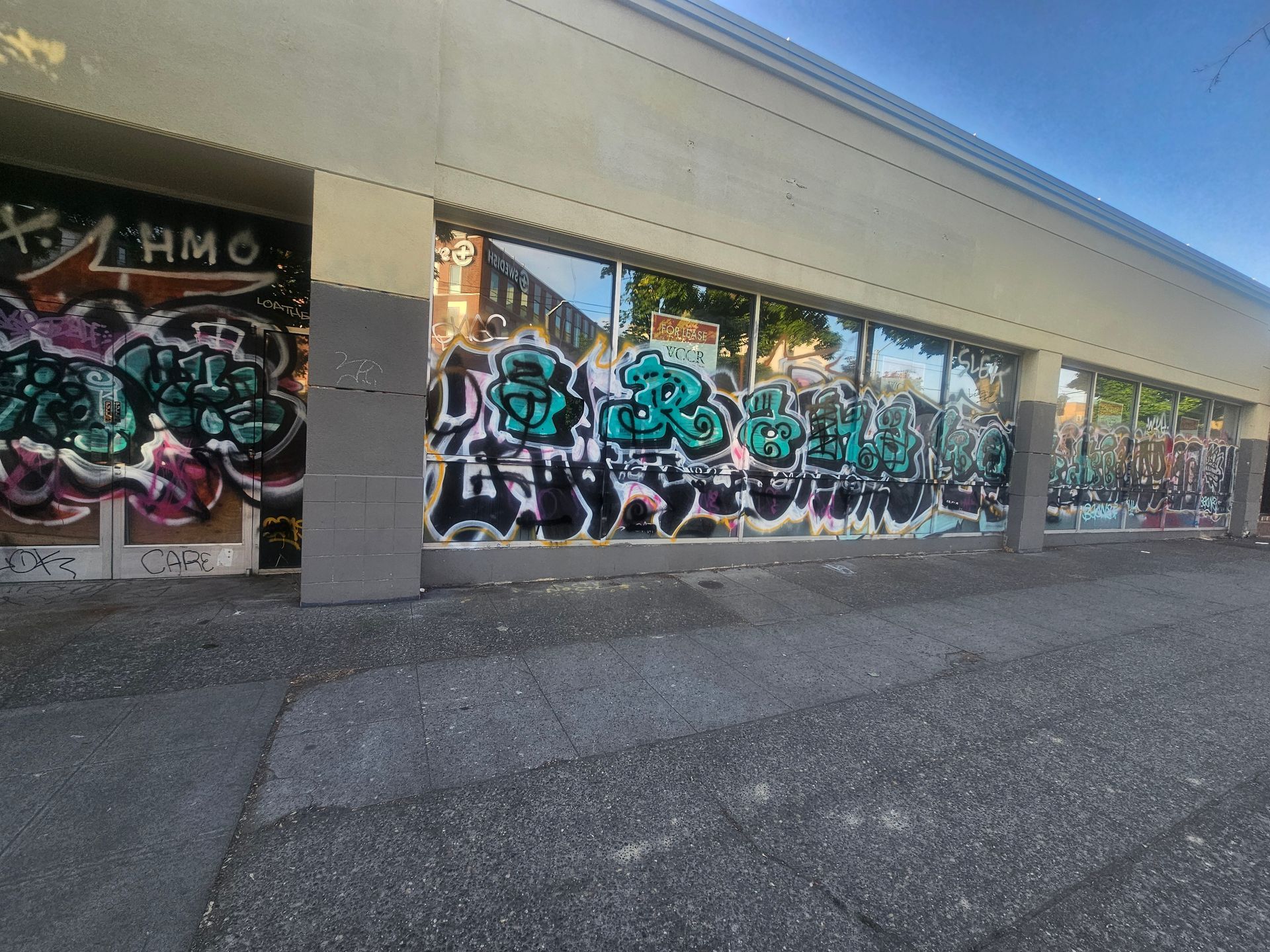 Graffiti-covered storefront on a city street. Multiple tags in black, teal, and pink.