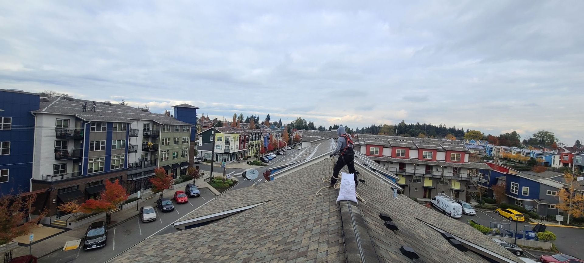 Person on a roof overlooking a city street with buildings and cars. Cloudy sky overhead.