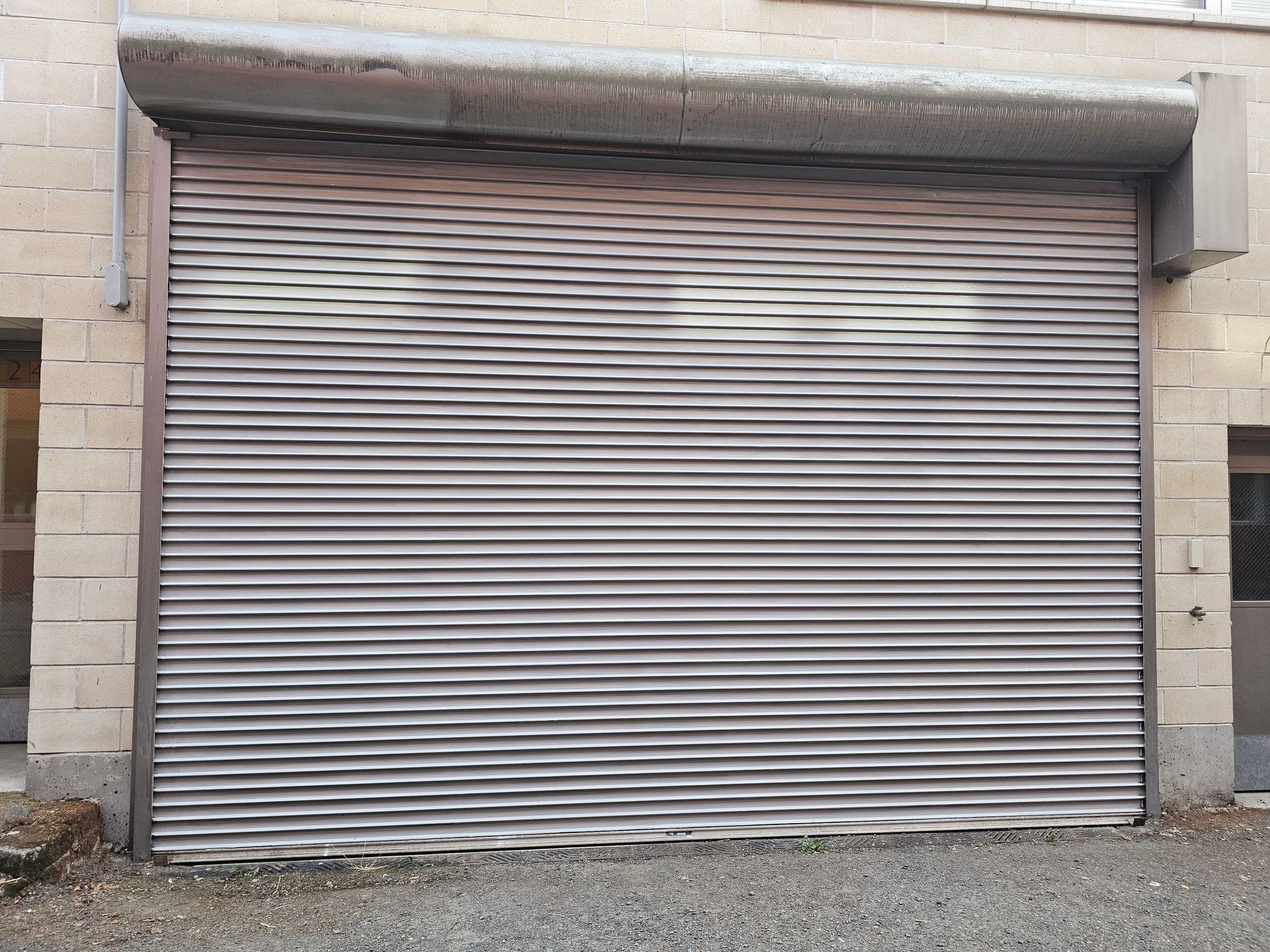 Closed gray roll-up security shutter on a brick building.