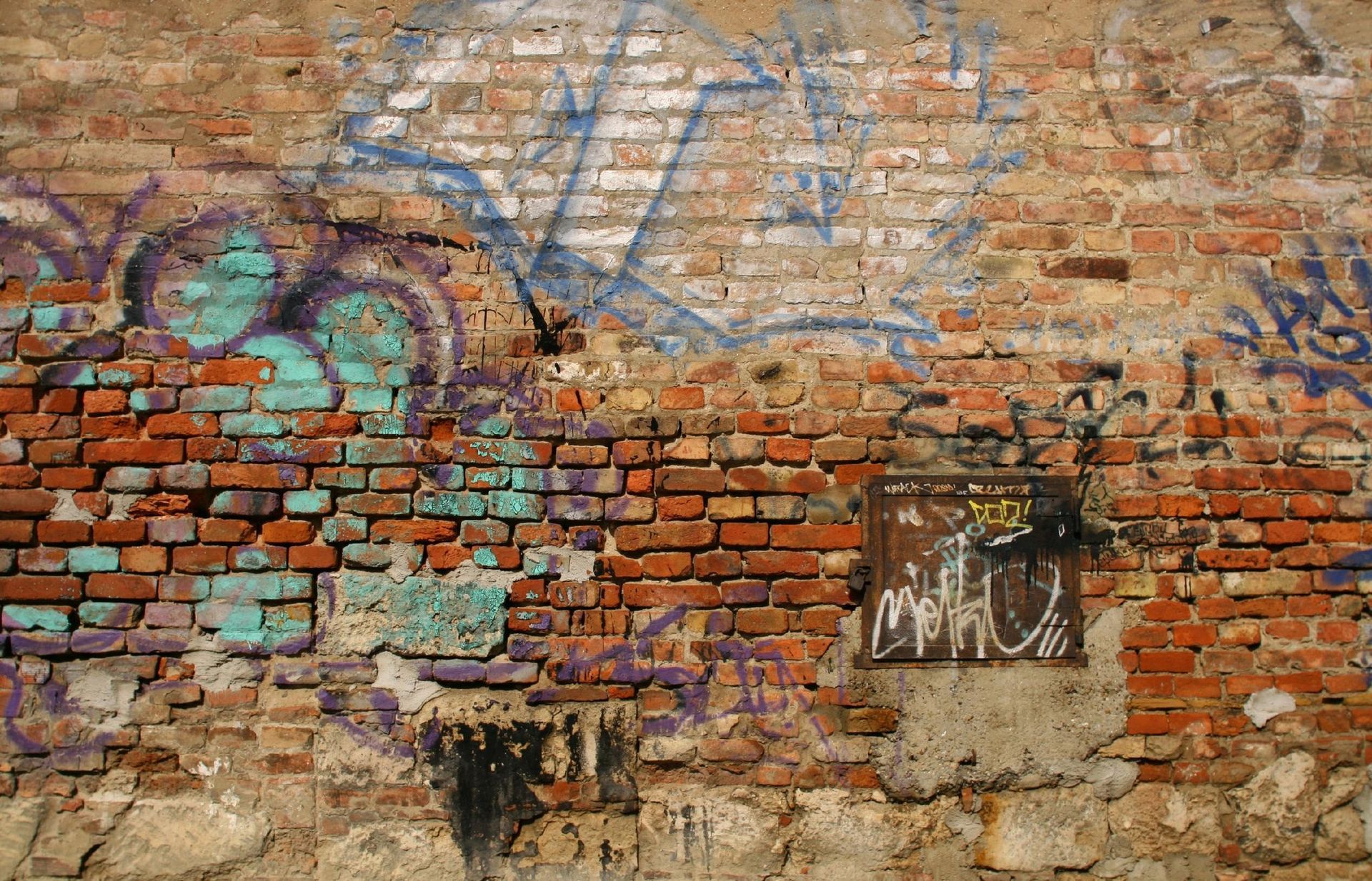 Weathered brick wall with graffiti in various colors.