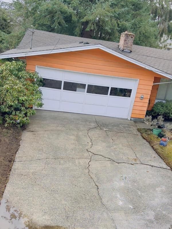 Concrete driveway leading to a house with an orange facade and white garage door.
