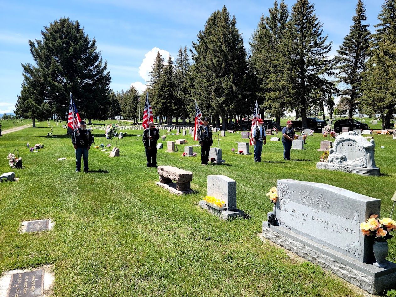People placing American flags on graves in a sunny cemetery.