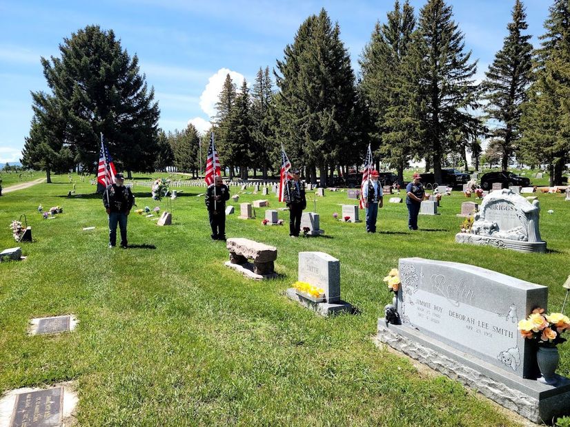 People placing American flags on graves in a sunny cemetery.