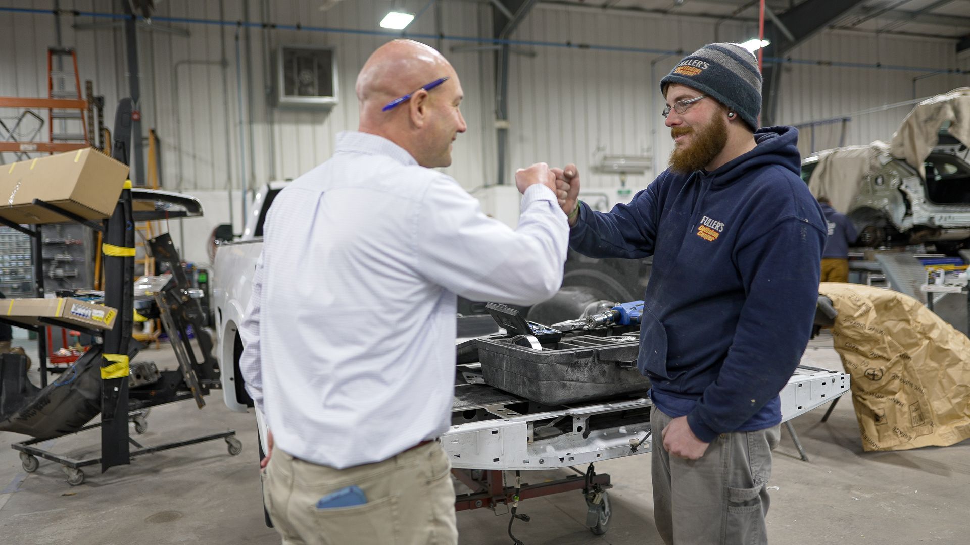 Two men are shaking hands in a garage in front of a truck.
