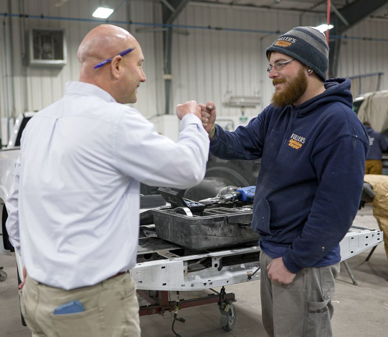 Two men are shaking hands in a garage in front of a truck.