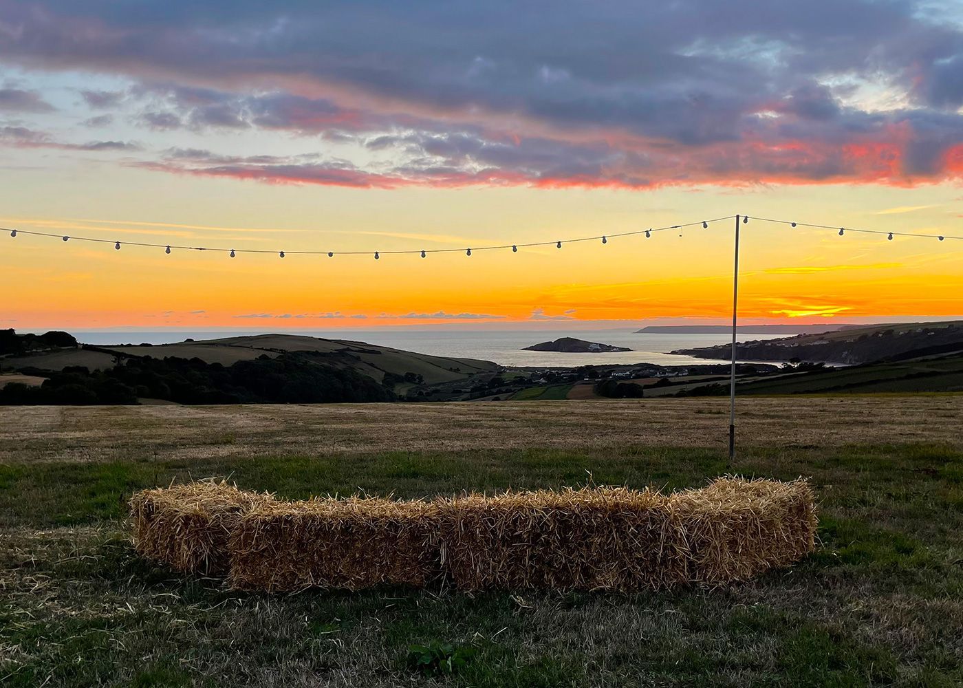A field of hay bales with a sunset in the background.