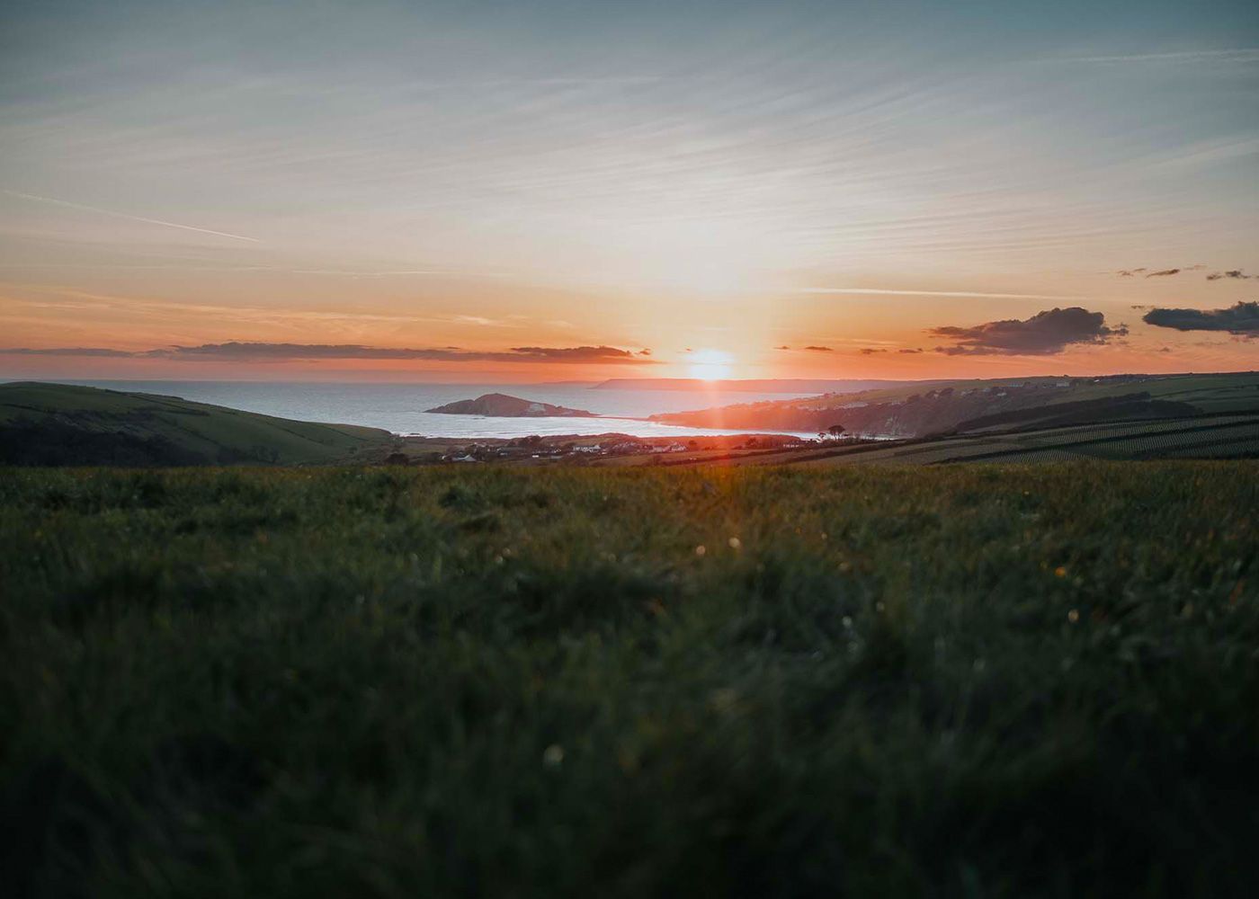 A sunset over a body of water with a grassy field in the foreground.