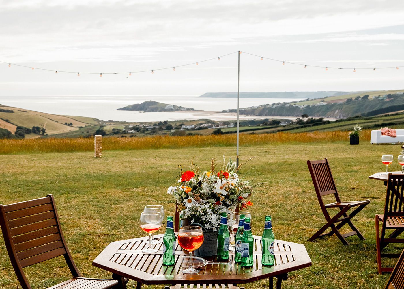 A table and chairs in a field with a view of the ocean.