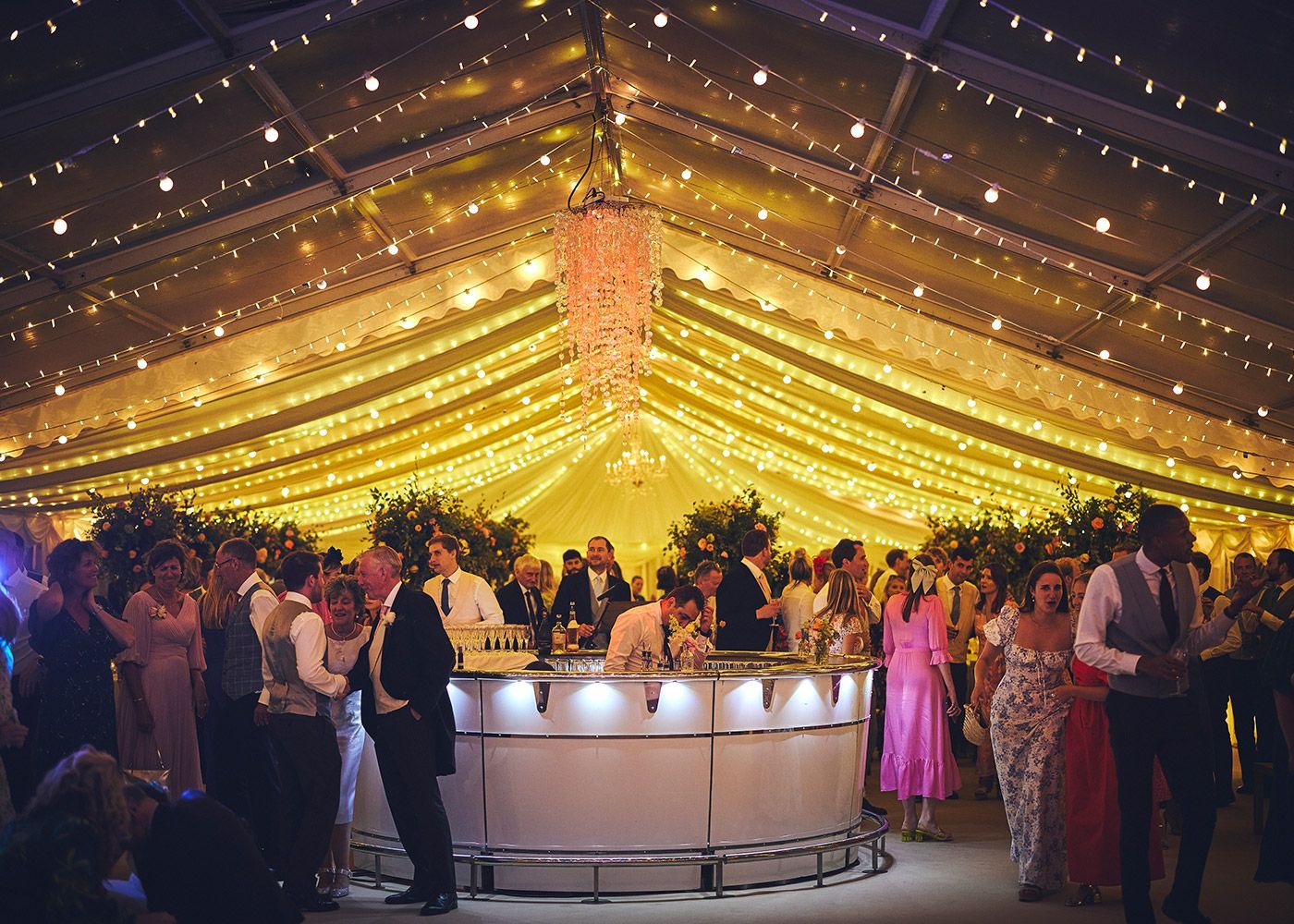 A large group of people are standing around a bar at a wedding reception.