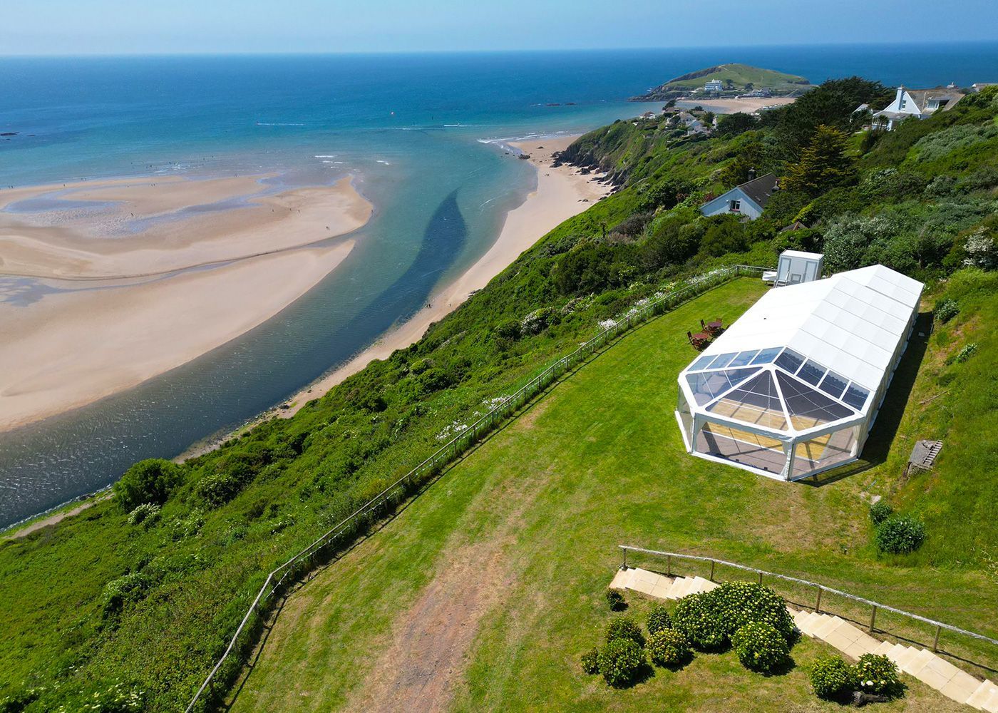 An aerial view of a large tent on a hill overlooking the ocean.