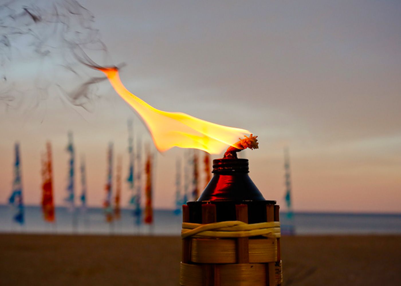 A torch is lit up on the beach at sunset