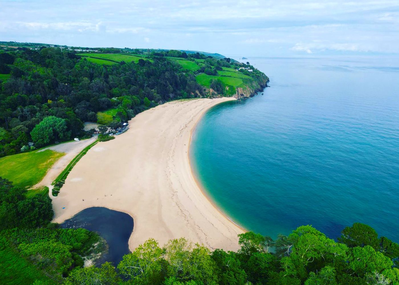 An aerial view of a beach surrounded by trees and a body of water.
