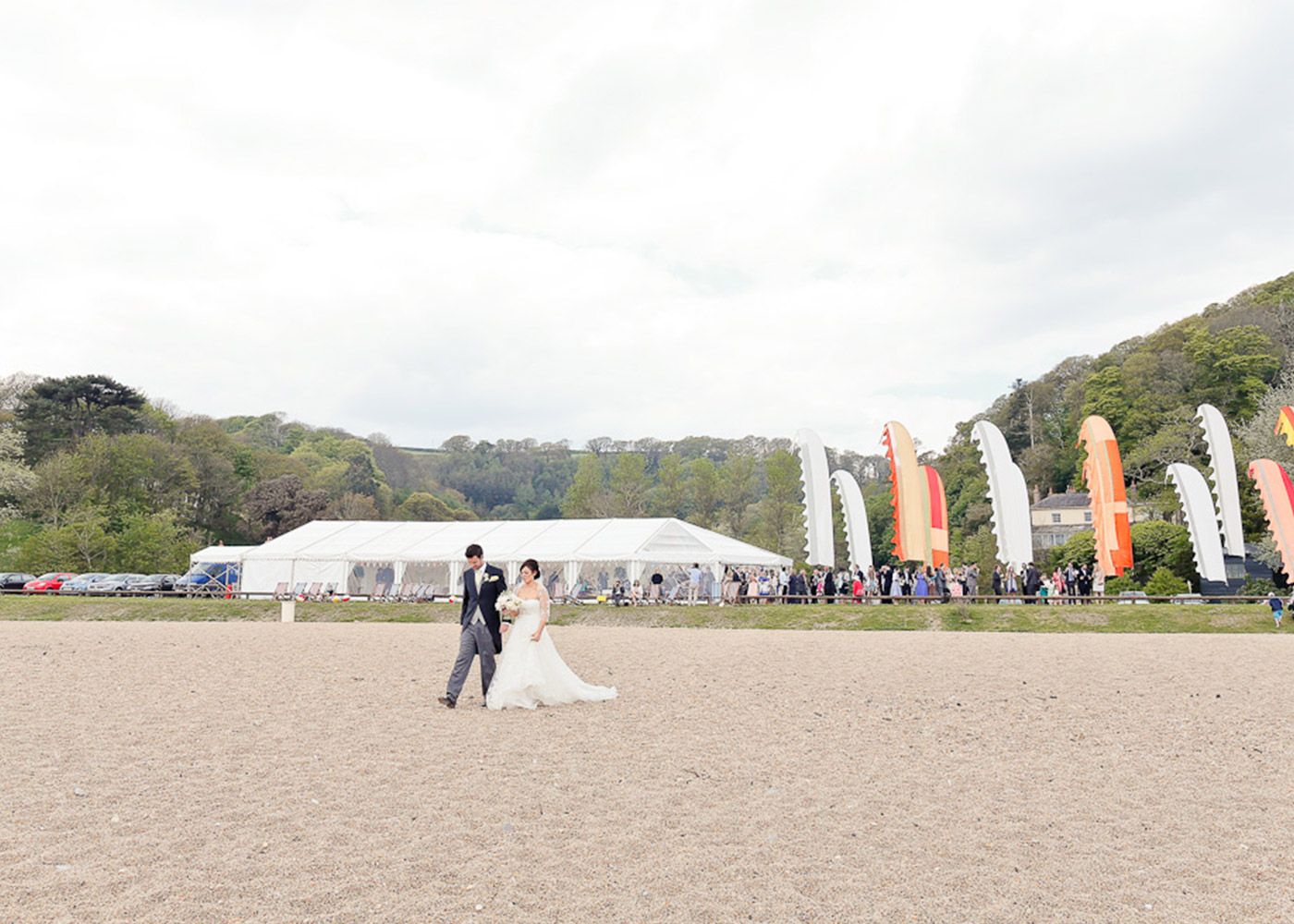 A bride and groom are walking on a sandy beach.