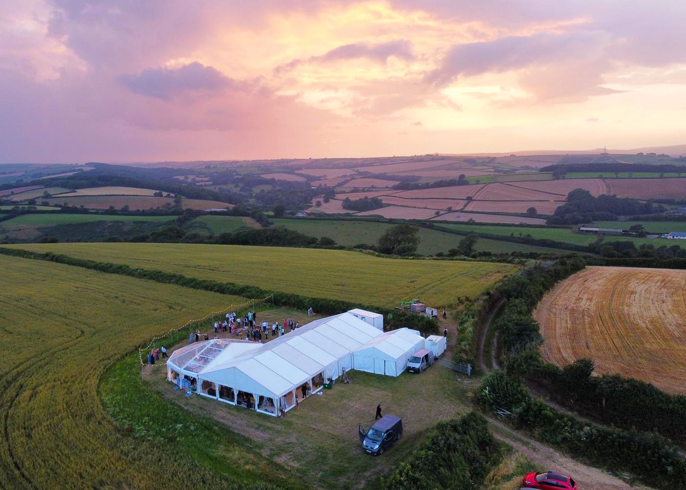 An aerial view of a large tent in the middle of a field at sunset.