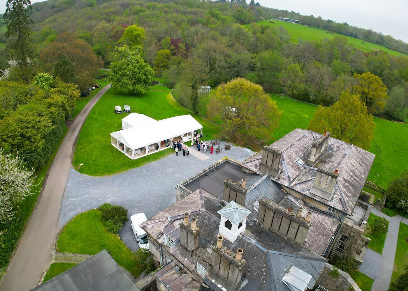 An aerial view of a large house with a white tent in the middle of a field.