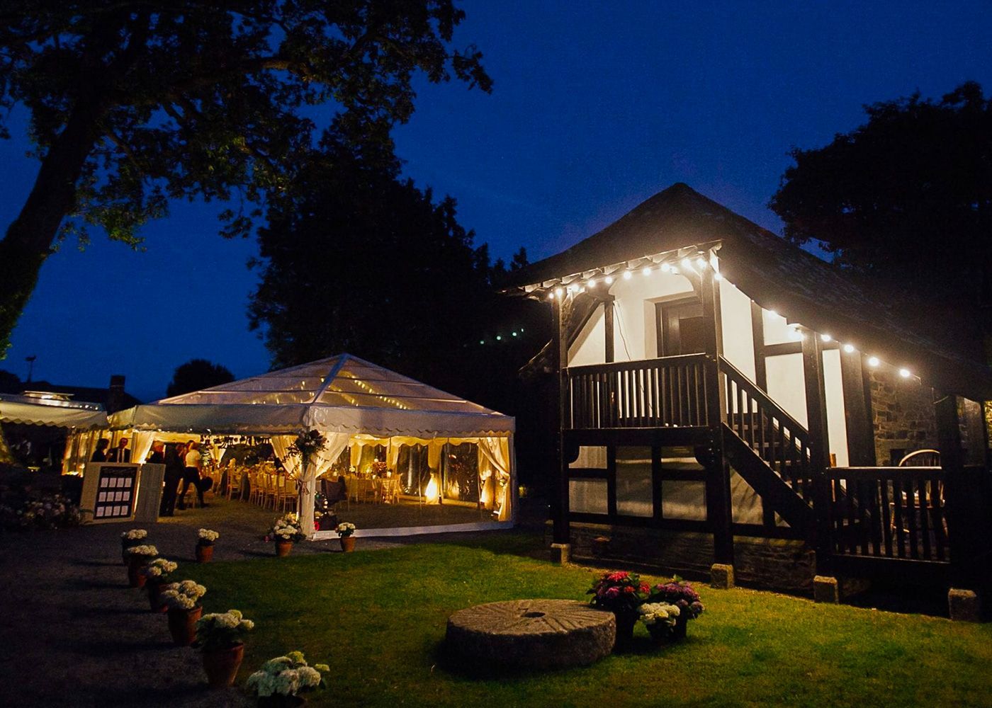 A large tent is lit up at night in front of a house.