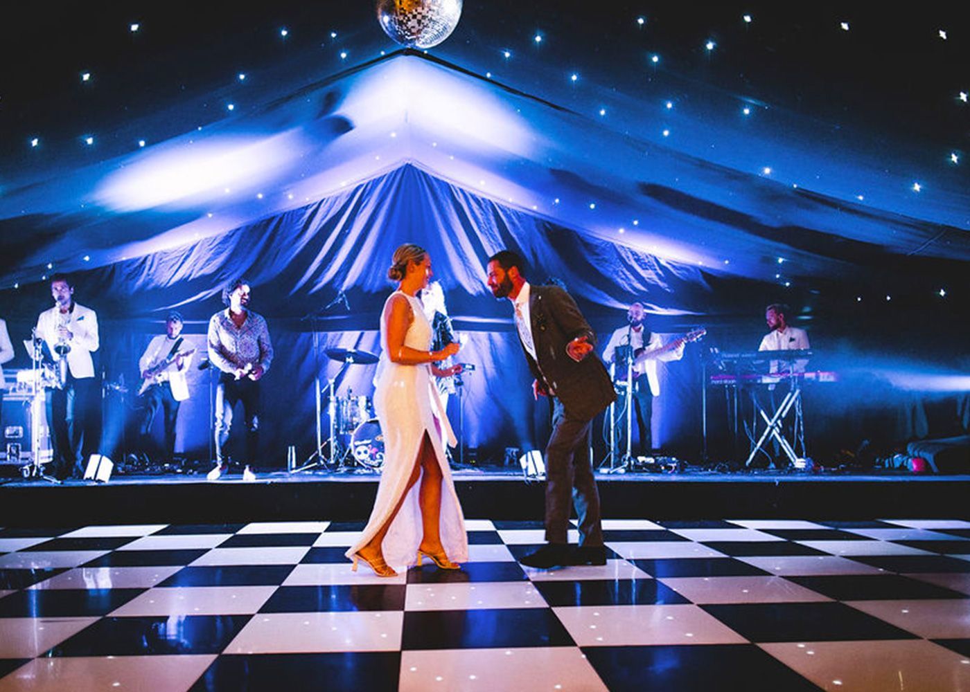 A bride and groom are dancing on a checkered dance floor.