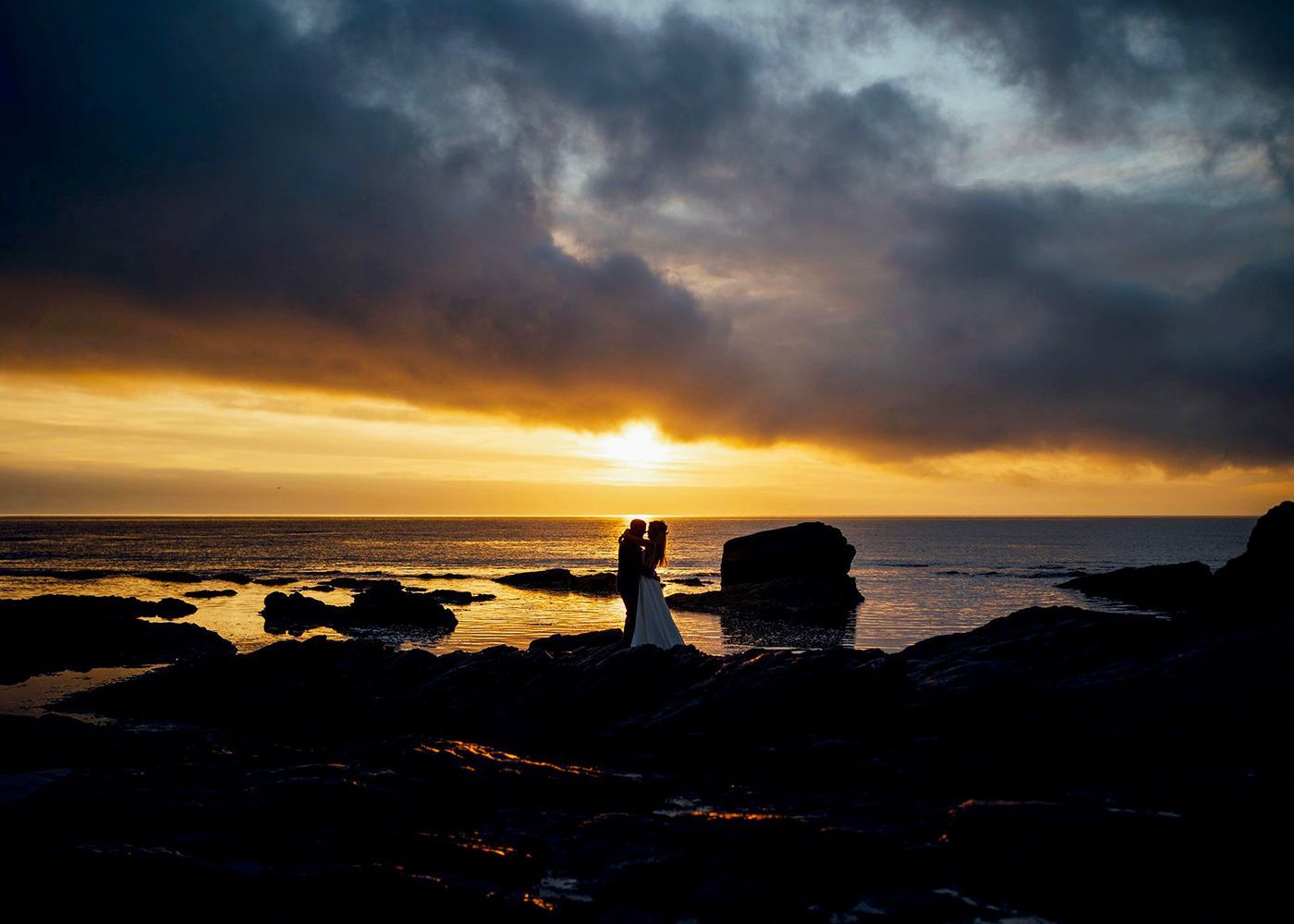 A bride and groom are kissing on the beach at sunset.