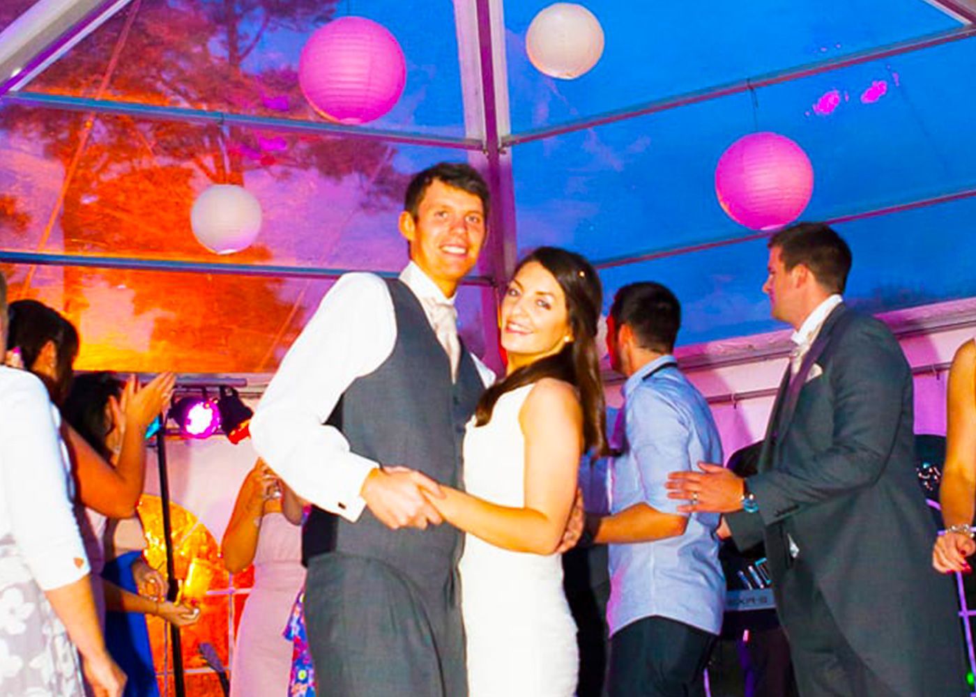 A bride and groom are dancing at a wedding reception under a clear tent.