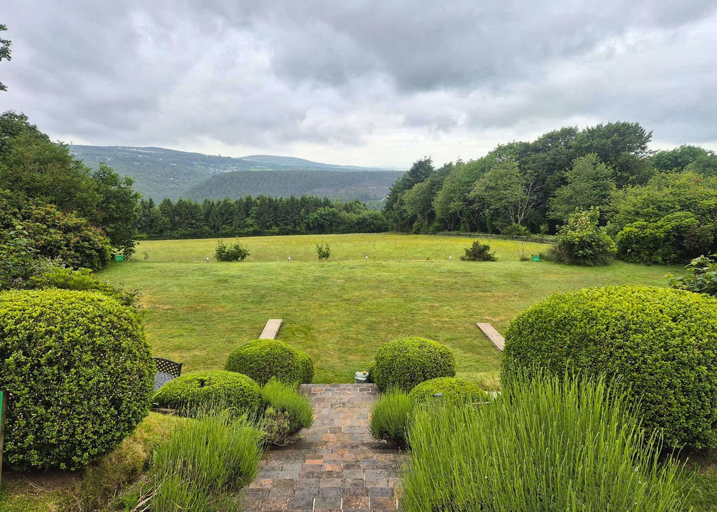 There is a path leading to a large grassy field with trees in the background.