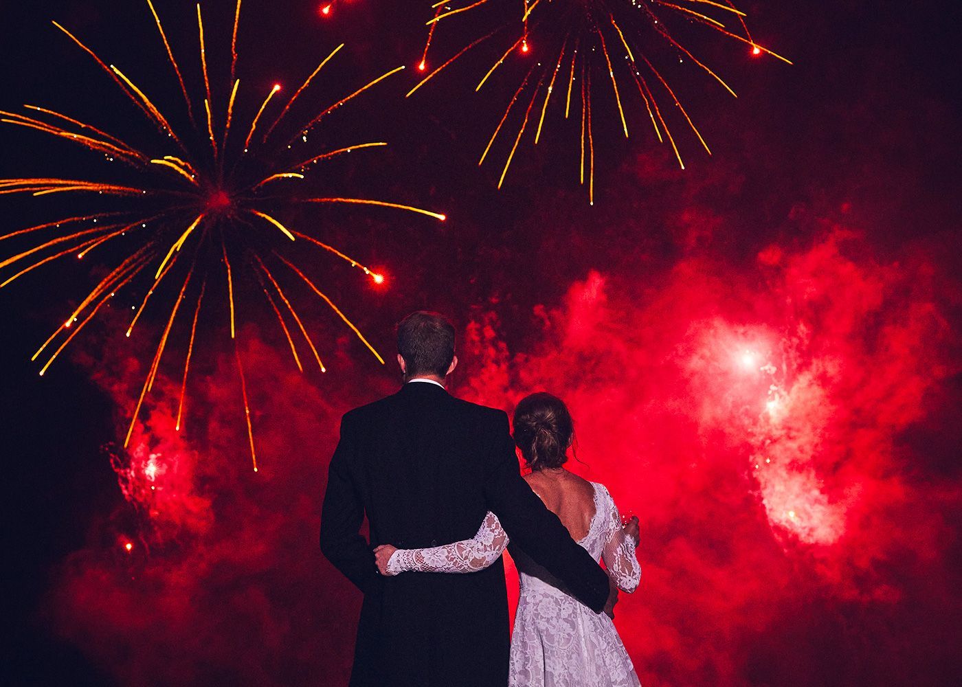 A bride and groom are standing in front of a fireworks display.
