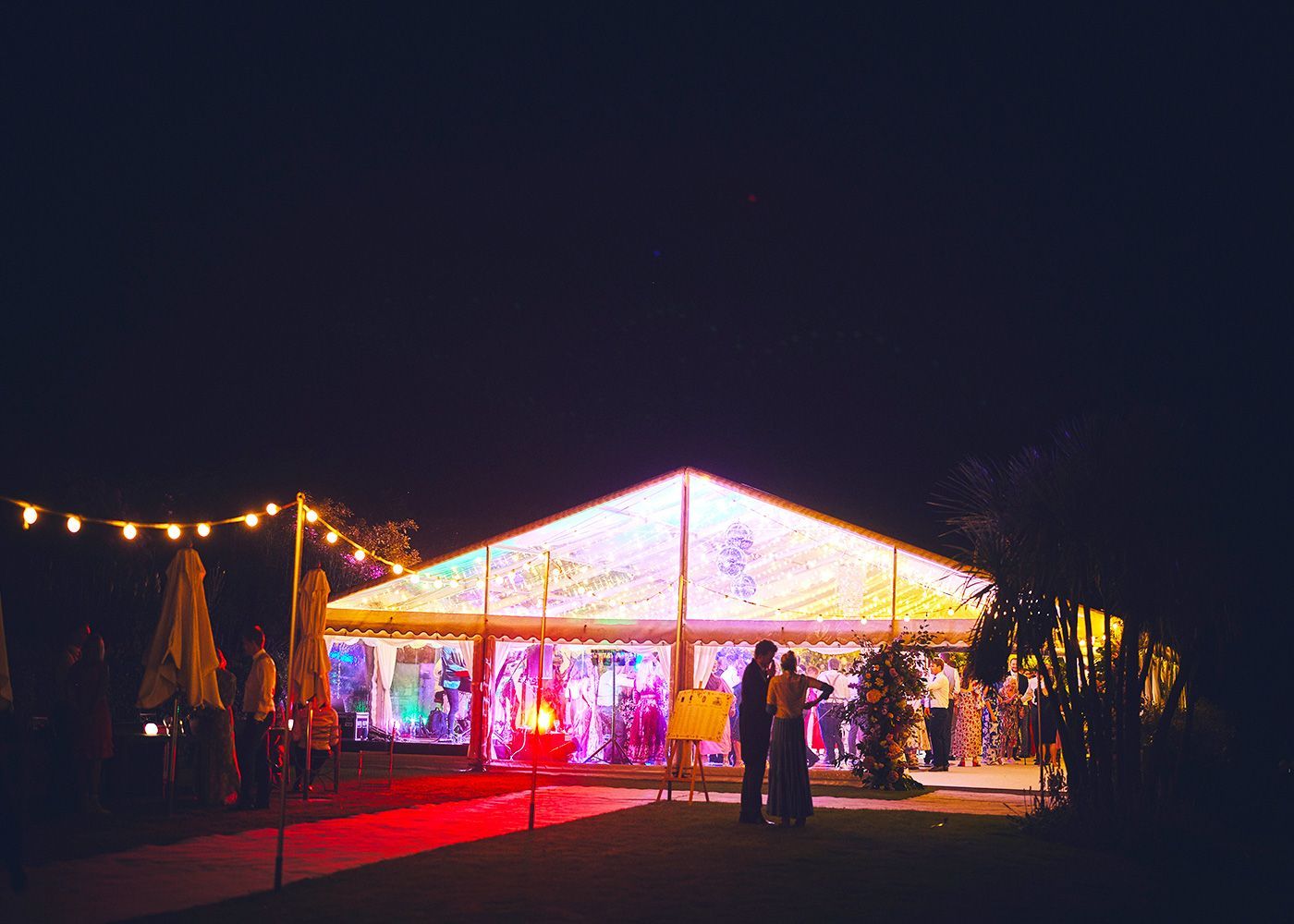 A large tent is lit up at night with a red carpet in front of it.