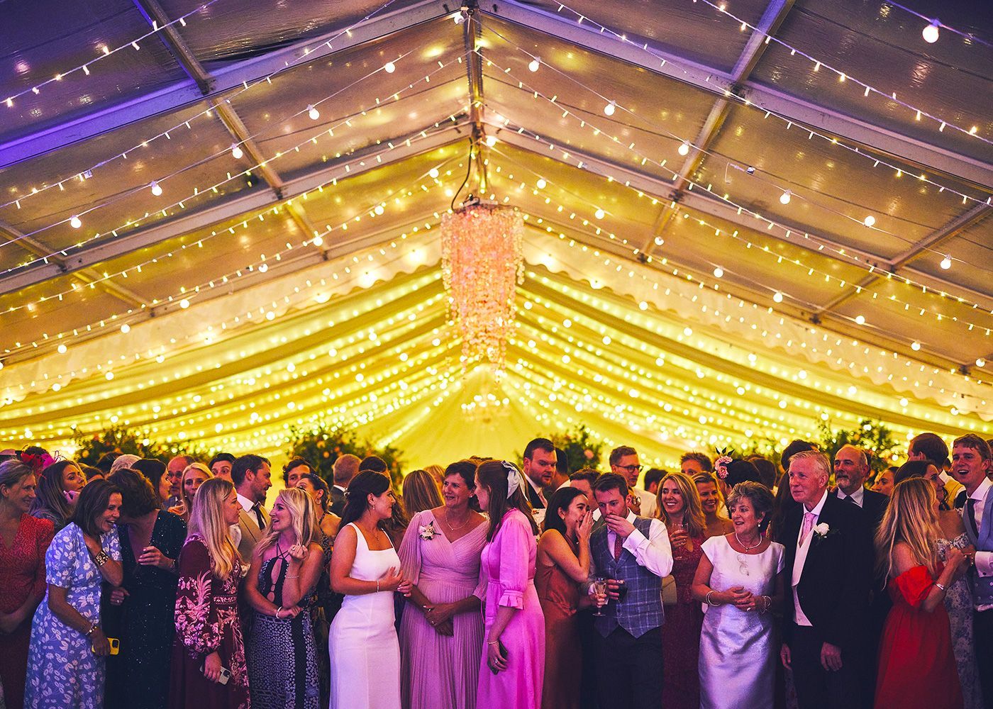A group of people are standing under a tent at a wedding reception.