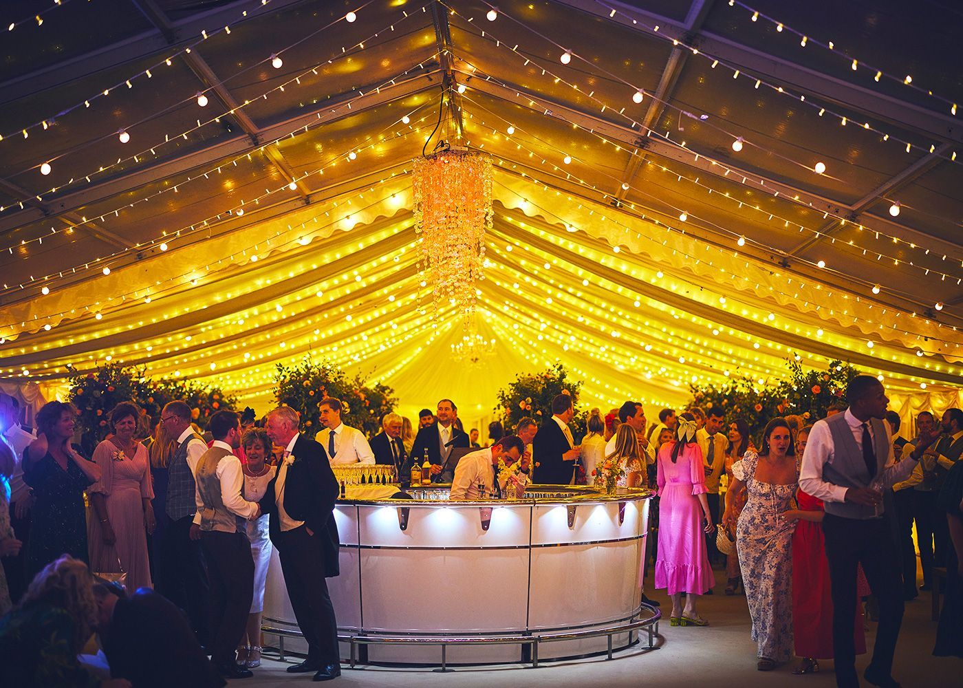 A large group of people are standing around a bar under a tent.