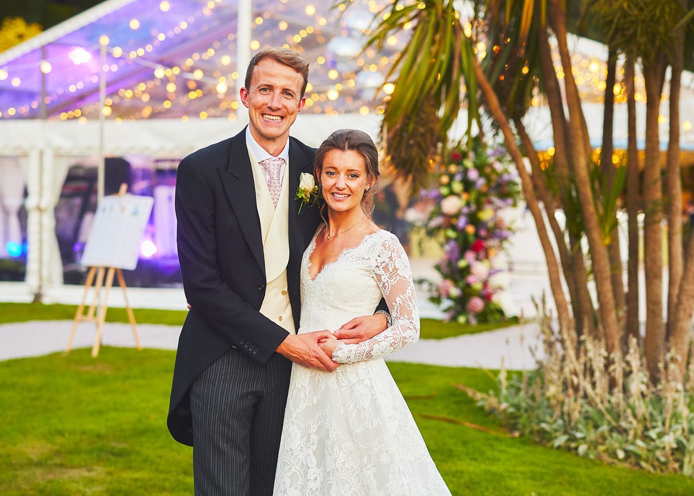 A bride and groom are posing for a picture in front of a clear tent.