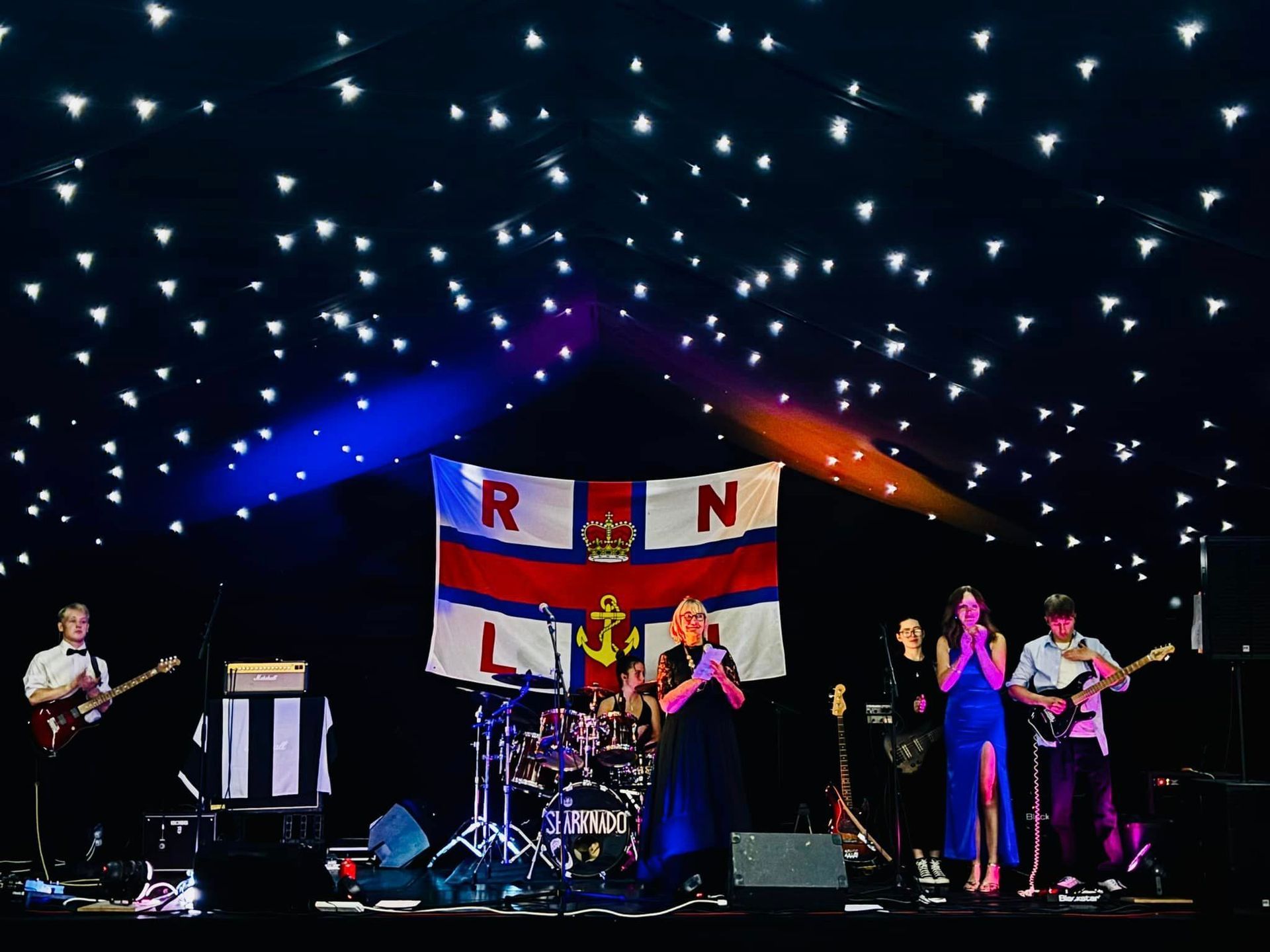 A group of people are standing on a stage in front of a flag.