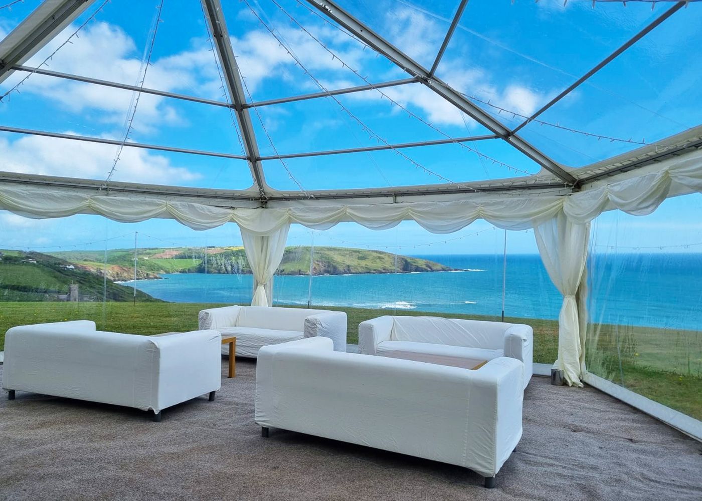A clear tent with white furniture and a view of the ocean.
