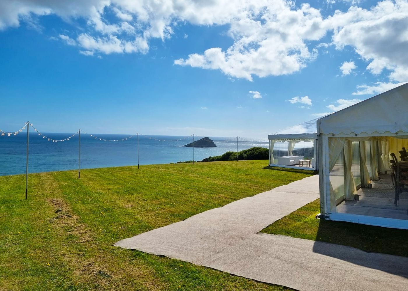 A white tent is sitting on top of a grassy hill overlooking the ocean.