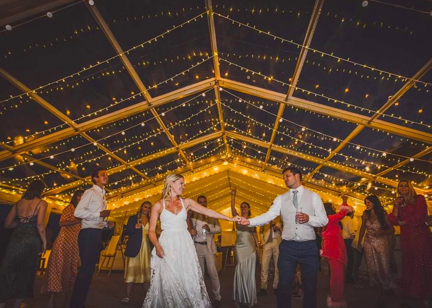 A bride and groom are dancing under a clear tent at their wedding reception.