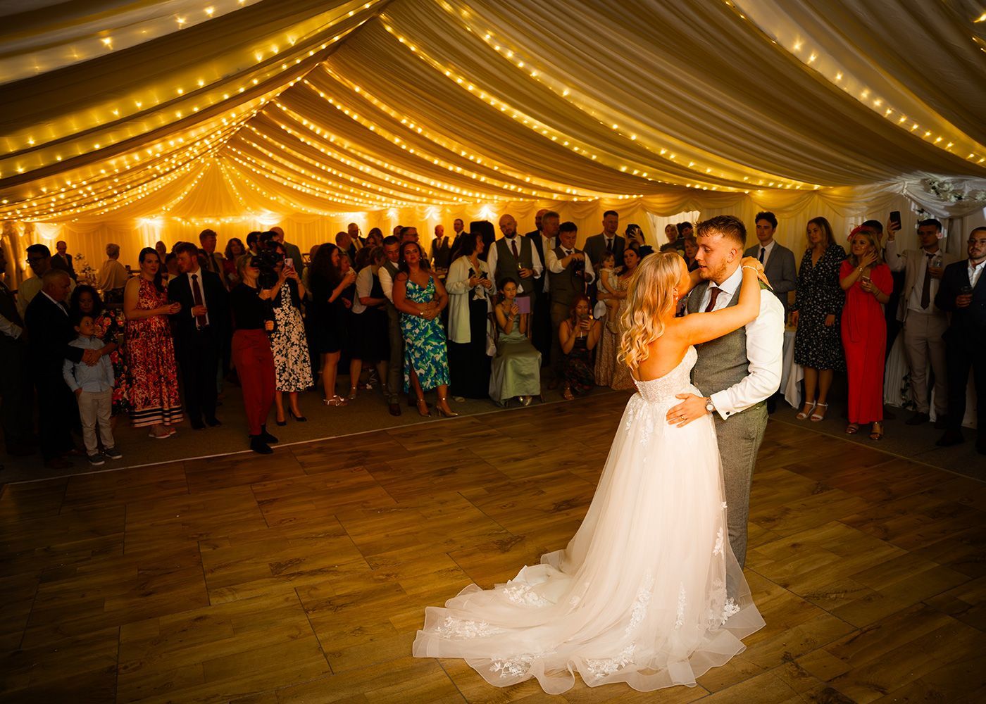 A bride and groom are dancing in a tent at their wedding reception.
